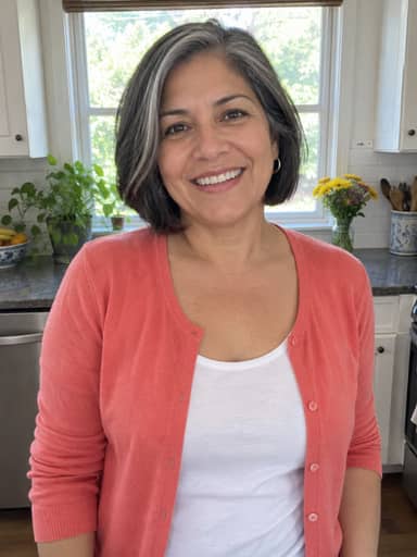 Uploaded photo: A kitchen photo in a coral cardigan. Same silver-streaked bob, showing off the stacked chairs and the gong.
