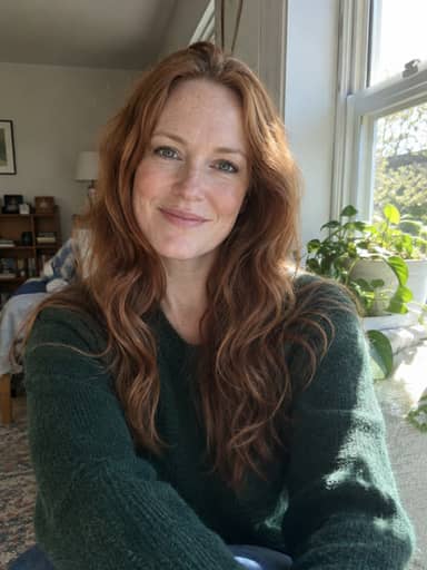 Uploaded photo: A window selfie in a green sweater. Same copper waves and freckles, with green star eyes.