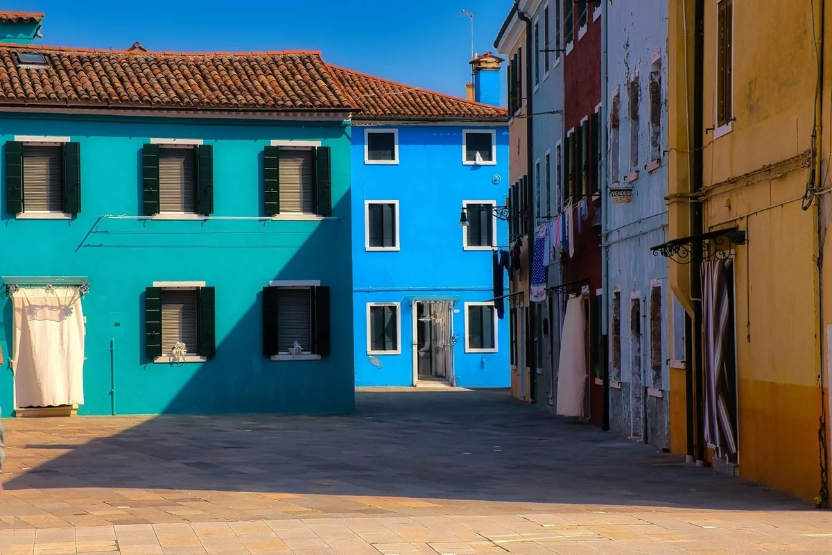 Four people walking past the coloured houses of Burano, removed from the photo